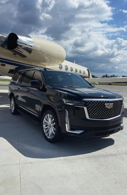 Luxury Black Cadillac Escalade at airport parked in front of a white private jet