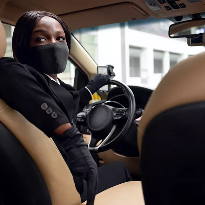 Lady Chauffeur in black suit sitting in the driving seat looking back