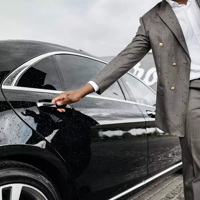 Chauffeur in grey suit opening door of a black luxury Mercedes S-class