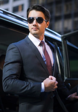 Chauffeur in nice suit standing with a luxury car