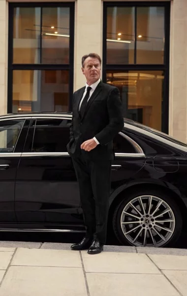 Chauffeur standing with a luxury black sedan waiting for the client