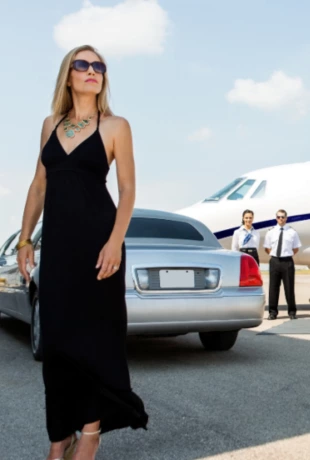 Woman out of a limo standing in front of the limo which is parked with a private jet